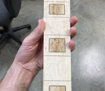 Hand holding an inlaid Elrick fretboard